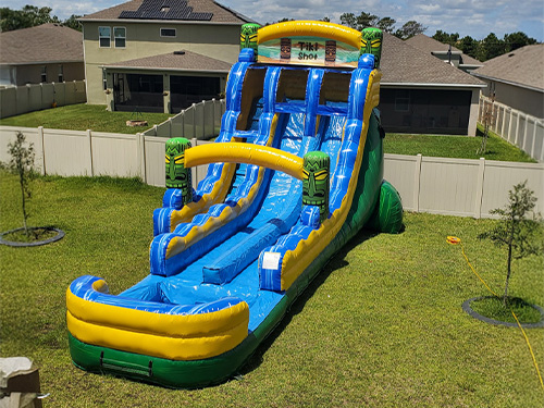 Tiki Shot tropical inflatable water slide rental set up in a backyard near Saint Cloud FL, long splash lane in bright blue and yellow